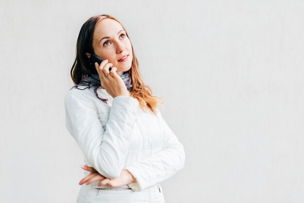 Portreta headshot patrzeje daleko od zamyślenie i opowiada na telefonie komórkowym młoda kobieta.