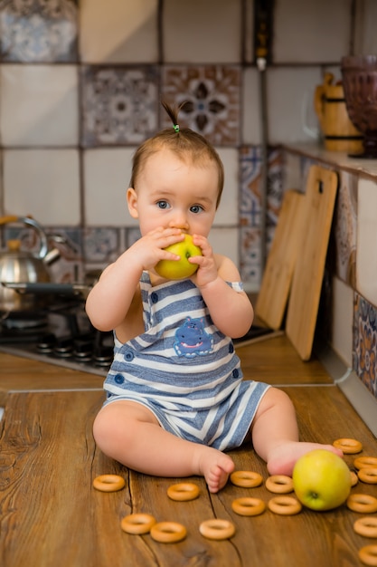 Portreta ono uśmiecha się śliczny dziecko w kithen. Dziecko siedzi w kuchni domu i ma jabłka i bułeczki