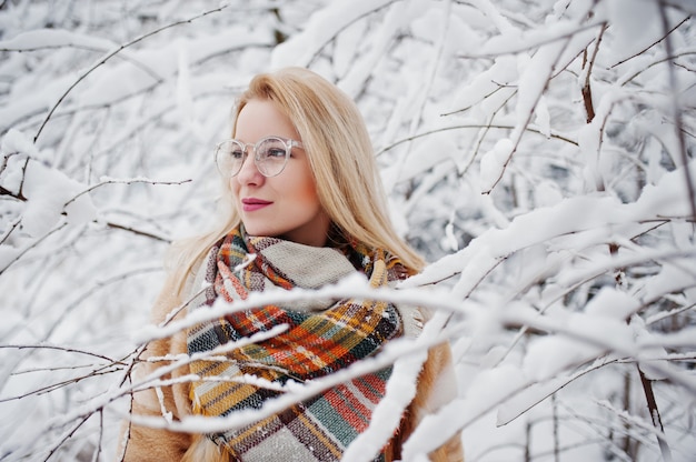 Portrety blondynki w okularach, czerwonym futrze i szaliku w zimowy dzień.