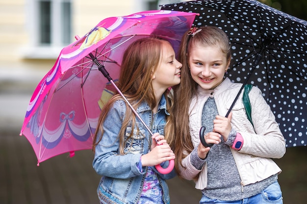 Portrety małych pięknych, stylowych dziewczynek szepczą plotki z parasolem w parku