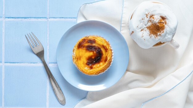 Portugalski deser Pastel de nata z kawą capuchino na niebieskiej płytce