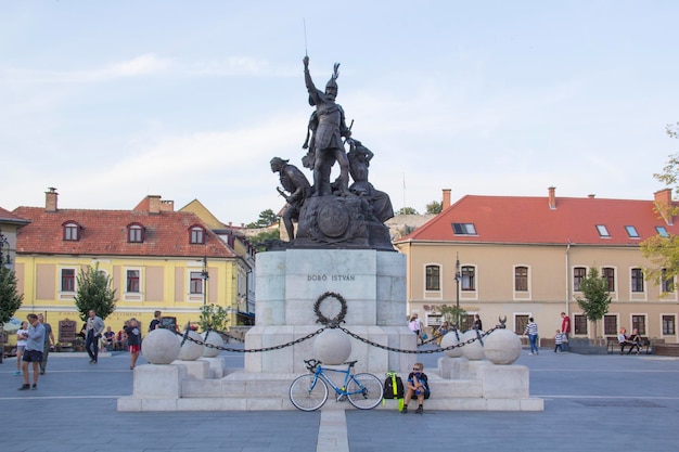 Posąg mężczyzny z niebieskim rowerem stoi przed budynkiem z błękitnym niebem.