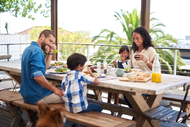 Posiłki zawsze smakują lepiej, gdy są spożywane z rodziną Ujęcie pięknej młodej rodziny cieszącej się wspólnym posiłkiem przy stole na świeżym powietrzu