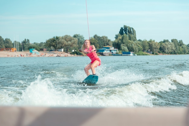 Postawa boczna. Piękna, aktywna młoda blondynka utrzymująca ciało w pozycji bocznej podczas jazdy na wakeboardzie