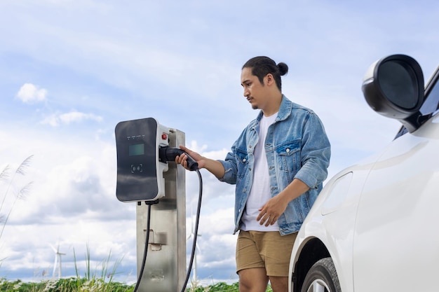 Postępowy człowiek ze swoim samochodem EV i turbiną wiatrową jako koncepcją energii odnawialnej