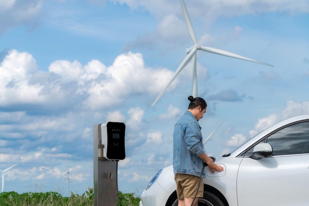 Postępowy człowiek ze swoim samochodem EV i turbiną wiatrową jako koncepcją energii odnawialnej