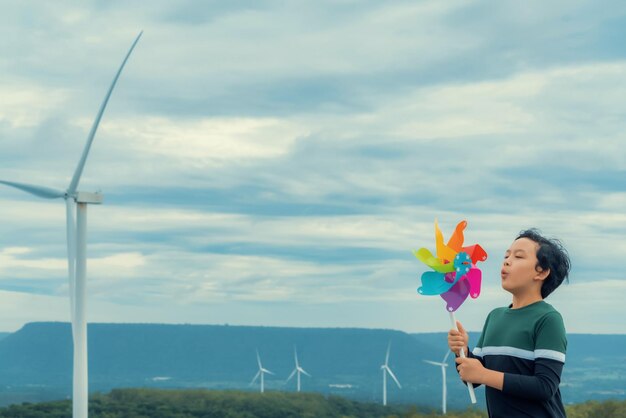 Postępowy młody azjatycki chłopiec bawiący się zabawką wiatraczek na farmie turbiny wiatrowej