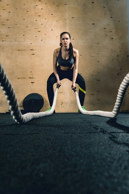 Potężna, atrakcyjna, muskularna kobieta trener CrossFit wykonuje trening walki na linach