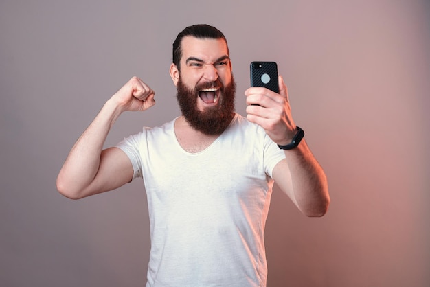 Potężny brodaty mężczyzna krzyczy głośno, patrząc na ekran telefonu