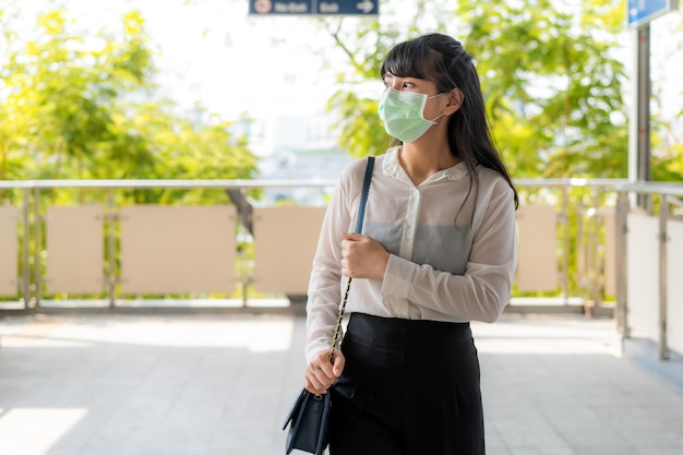 Potomstwa stresują się Azjatycki bizneswoman w białej koszula iść pracować w zanieczyszczeniu mieście jest ubranym maskę ochronną zapobiega pyłu PM2.5, smogowi, zanieczyszczeniu powietrza i COVID-19 w Bangkok, Tajlandia.