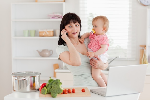 Powabna brunetki kobieta na telefonie podczas gdy trzymający jej dziecka w jej rękach