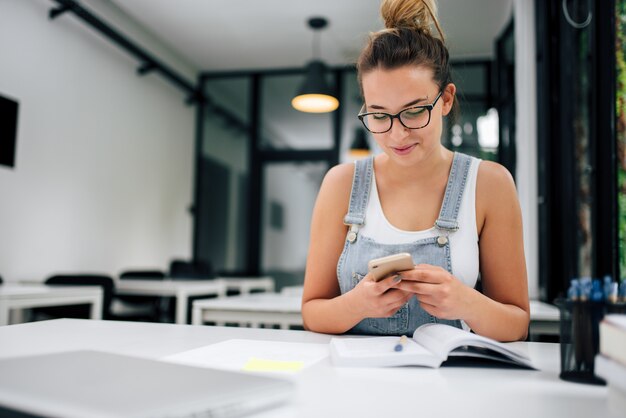 Powabna dziewczyna w eyeglasses używać telefon indoors.