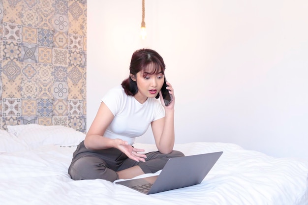 Poważna azjatycka piękna dziewczyna pracuje na laptopie w łóżku Praca w domu koncepcja