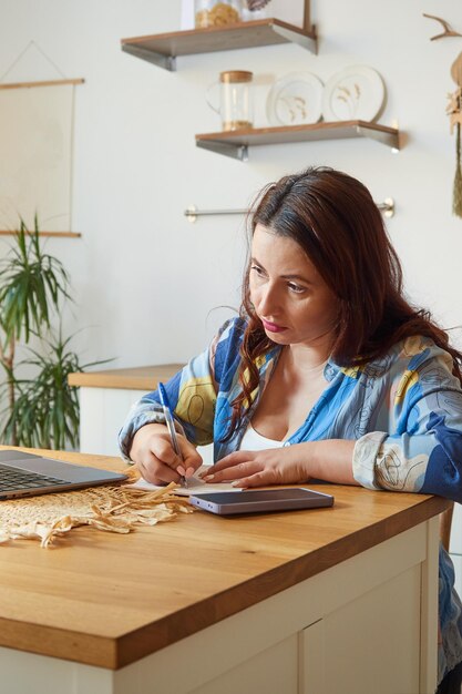 Poważna freelancerka robiąca notatki na papierze, patrząc na laptopa Zdalne uczenie się wideokonferencji