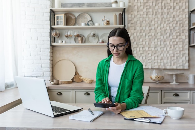 Poważna i skupiona bizneswoman freelancer na papierkowej robocie w domu w kuchni brunetka w okularach