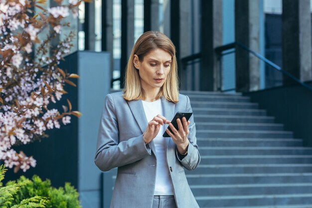 Poważna I Zamyślona Kobieta Biznesu Korzysta Z Telefonu Poza Biurem, Patrząc Na Ekran Smartfona