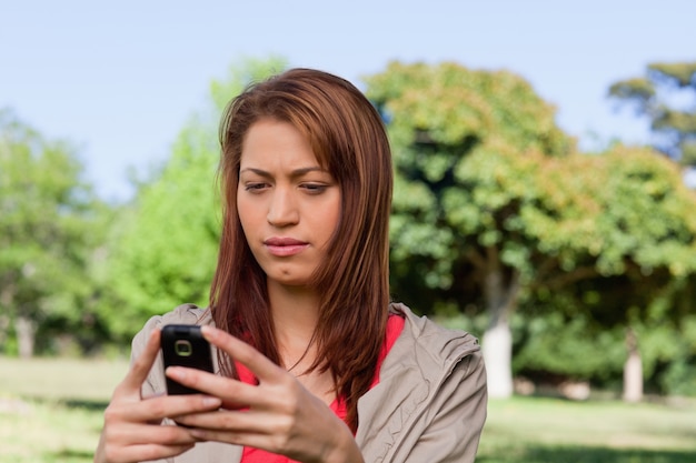 Poważna kobieta czyta wiadomość tekstową w jaskrawym obszar trawiasty