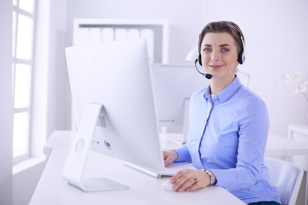 Poważna ładna młoda kobieta pracująca jako operator telefoniczny z zestawem słuchawkowym w biurze