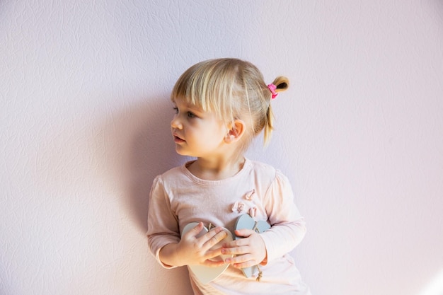 Poważna mała dziewczynka Mała dziewczynka o blond włosach trzyma w dłoniach dwa drewniane, białe serca