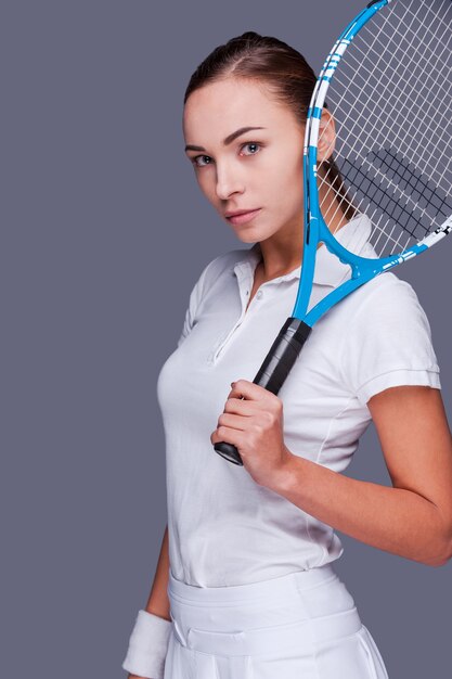Poważna rywalizacja. Piękne młode kobiety w sportowych ubraniach trzymające rakietę tenisową na ramieniu