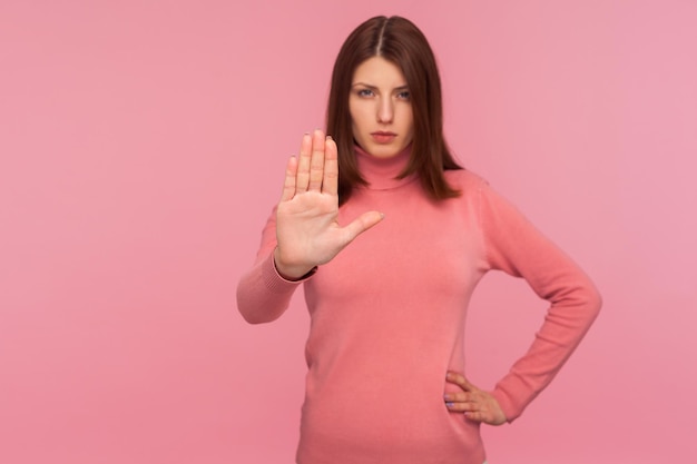 Poważna zaniepokojona kobieta o brązowych włosach pokazująca gest zakazu zatrzymania z ostrzeżeniem dłoni Wewnątrz strzał studio na białym tle na różowym tle