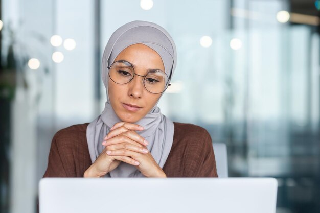 Poważna znudzona bizneswoman w biurze muzułmanka w hidżabie myśli siedząc w miejscu pracy
