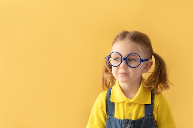 Poważne dziecko w wieku szkolnym w okularach na białym tle na żółtym tle, patrząc na miejsce na kopię Powrót do szkoły