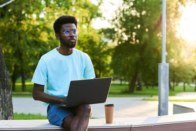 Poważny afrykański biznesmen pracujący online na laptopie, siedząc w parku na świeżym powietrzu