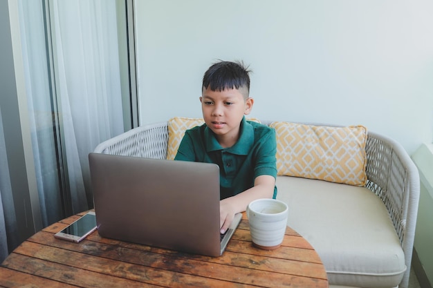 Poważny azjatycki chłopiec odrabiający lekcje za pomocą laptopa