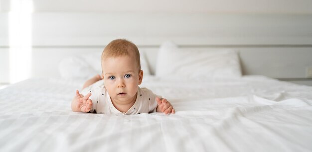 poważny, biały, kaukaski chłopczyk o niebieskich oczach, sześciomiesięczny leżący na łóżku i patrzący w kamerę, prosty widok, szczęśliwe dzieciństwo