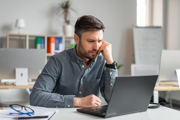 Poważny Biznesmen W średnim Wieku, Korzystający Z Laptopa I Czytający Raporty, Siedzący W Miejscu Pracy W