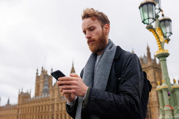 Poważny brodaty mężczyzna ze smartfonem w dłoniach na ulicy Londynu