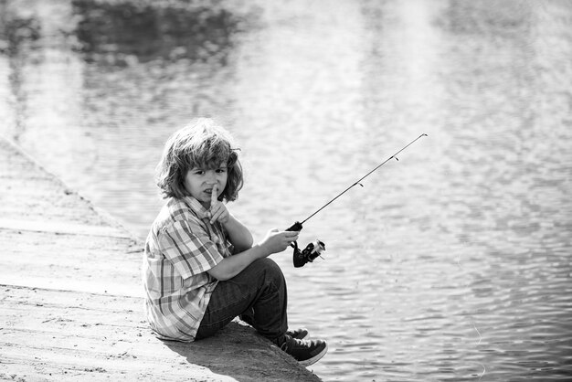 Poważny chłopczyk łowi na rzece wędkę.