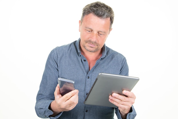 Poważny mężczyzna pracownik za pomocą tabletu i patrząc na telefon komórkowy na białym tle studio