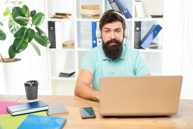 Poważny mężczyzna słucha webinaru w słuchawkach za pomocą laptopa w biurowej edukacji online