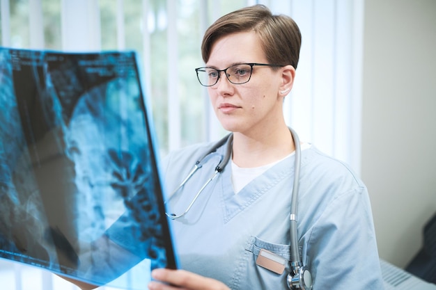 Poważny młody chirurg rasy kaukaskiej ze stetoskopem na szyi, pracujący z tomografią komputerową pacjenta w szpitalu