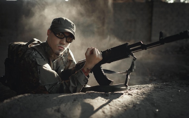 Poważny Młody żołnierz Niepodległego Państwa W Mundurze Kamuflażowym Z Dużym Plecakiem Na Plecach W Okularach Taktycznych I Czapce Przeładowuje Karabin Maszynowy W Ukryciu