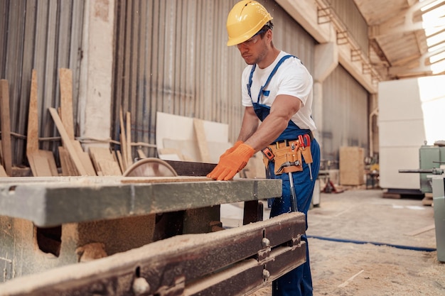 Poważny pracownik płci męskiej używający sprzętu do obróbki drewna w warsztacie