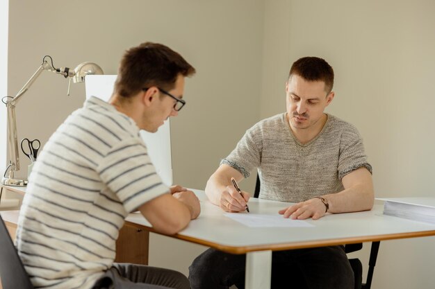 Poważny profesjonalista konsultujący klienta w biurze Dwóch mężczyzn odbywających spotkanie nawiązujące rozmowę biznesową Ubezpieczyciel udzielający porad kierownik składający ofertę Mentor nauczający stażysta Rozmowa kwalifikacyjna