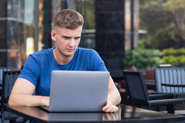 Poważny Przystojny Sfrustrowany Zdenerwowany Facet, Freelancer, Młody Smutny Skoncentrowany Mężczyzna Pracujący Na Laptopie, Komputer W Kawiarni Na świeżym Powietrzu. Niezależna Koncepcja Pracy Na Odległość. Chłopiec Dostał Złe Wieści, Patrząc Na Ekran