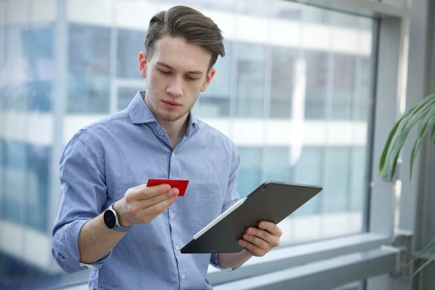 Poważny, skoncentrowany, skoncentrowany facet, młody człowiek, robiący zakupy w Internecie online na swoim komputerze typu tablet laptop