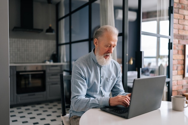 Poważny starszy mężczyzna w średnim wieku pracujący na laptopie w domu Przystojny starszy mężczyzna dojrzały użytkownik patrząc na ekran komputera komunikowania się online