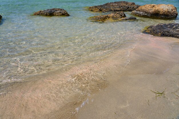 Powierzchnia Czystej Wody Na Tropikalnej, Piaszczystej Plaży Z Kamieniami W Grecji Na Krecie.