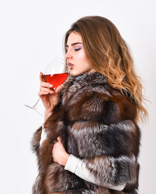 Powody Piją Czerwone Wino Zimą. Kobieta Pije Wino. Dziewczyna Moda Makijaż Nosić Futro Trzymać Szklany Alkohol. Elitarny Wypoczynek. Lady Fashion Model Kręcone Fryzury Cieszą Się Elitarnym Winem. Koncepcja Kultury Wina.