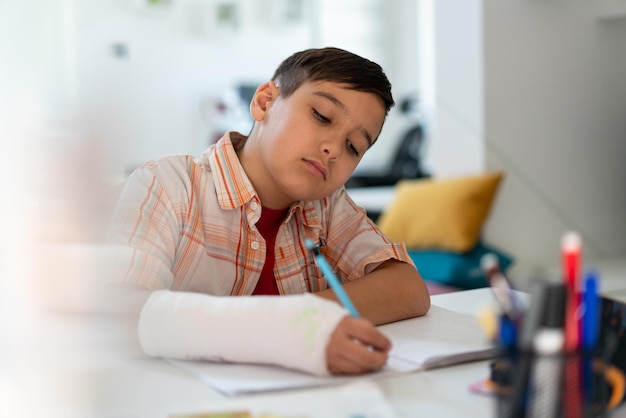 Powrót do szkoły myślące dziecko chłopiec pisze rysunek w zeszycie siedząc przy biurku i odrabiając pracę domową