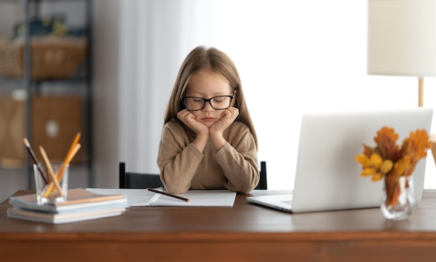 Powrót do szkoły. Myślące dziecko siedzi przy biurku. Dziewczyna odrabiania lekcji lub edukacji online.