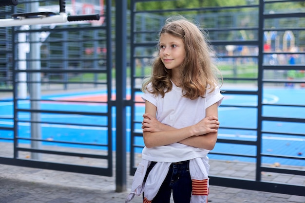 Powrót do szkoły, portret pewnie dziecko dziewczynka 8, 9 lat w pobliżu szkolnego boiska do koszykówki. Początek studiów, sport, przekazywanie nowej wiedzy i umiejętności