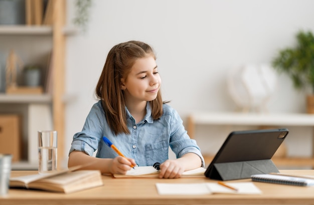 Powrót do szkoły. Szczęśliwe dziecko siedzi przy biurku. Dziewczyna odrabiania lekcji lub edukacji online.