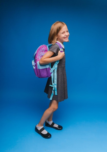 Powrót do szkoły Uczennica z tornisterem na odosobnionym niebieskim tle studia Mała dziewczynka trzyma plecak