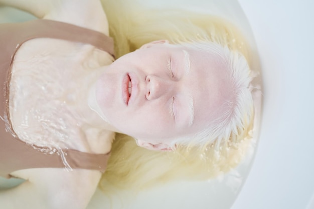 Powyżej ujęcie młodej kobiety albinos bez makijażu leżącej w wannie